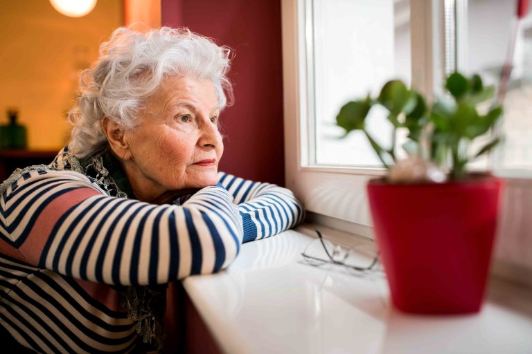 Sad alone senior woman looking through window Sad alone senior woman looking through window