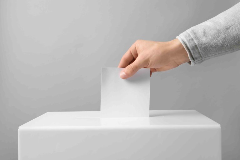 Man putting his vote into ballot box on light background, closeu Man putting his vote into ballot box on light background, closeu