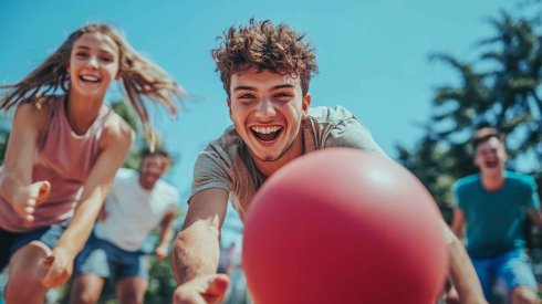 Spaß bei Freizeiten Mehrere Jugendliche mit einem roten Ball, die Spaß haben und in die Kamera lachen.