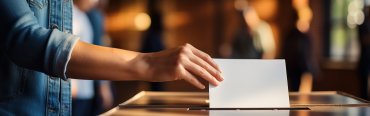Hand of a woman voting at a ballot box during elections Hand, die einen Umschlag mit Wahlunterlagen in die Wahlurne einwirft.