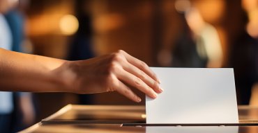 Hand, die einen Umschlag mit Wahlunterlagen in die Wahlurne einwirft.