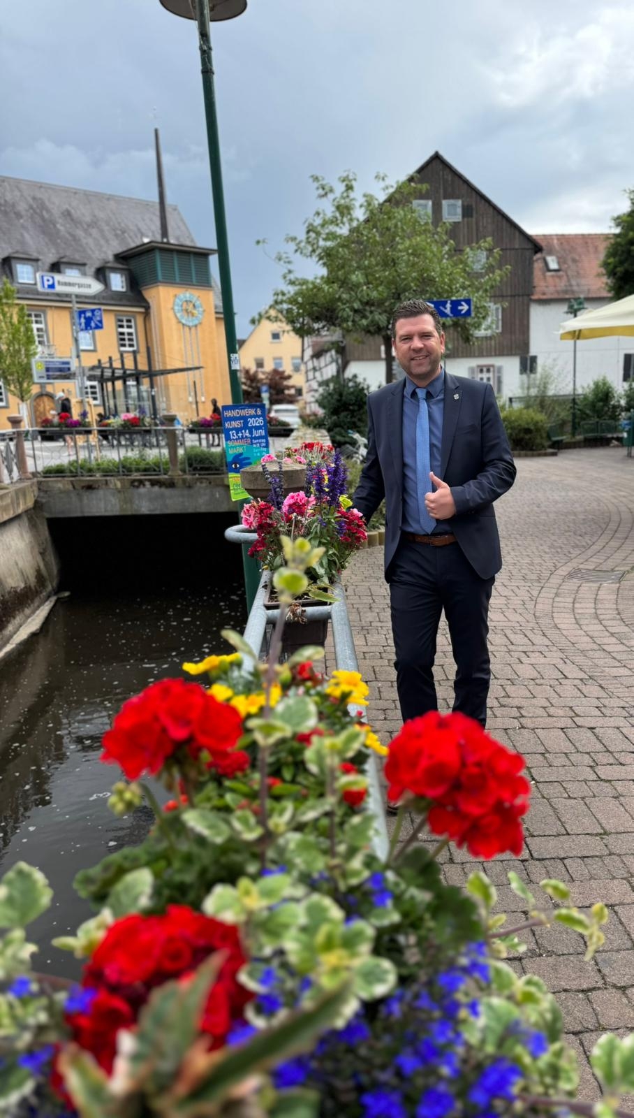 Bürgermeister Silbereis vor der schönen Bepflanzung entlang der Modau Lächelnder Mann im Anzug spaziert entlang eines mit Blumen geschmückten Bachlaufs durch einen Ortskern.