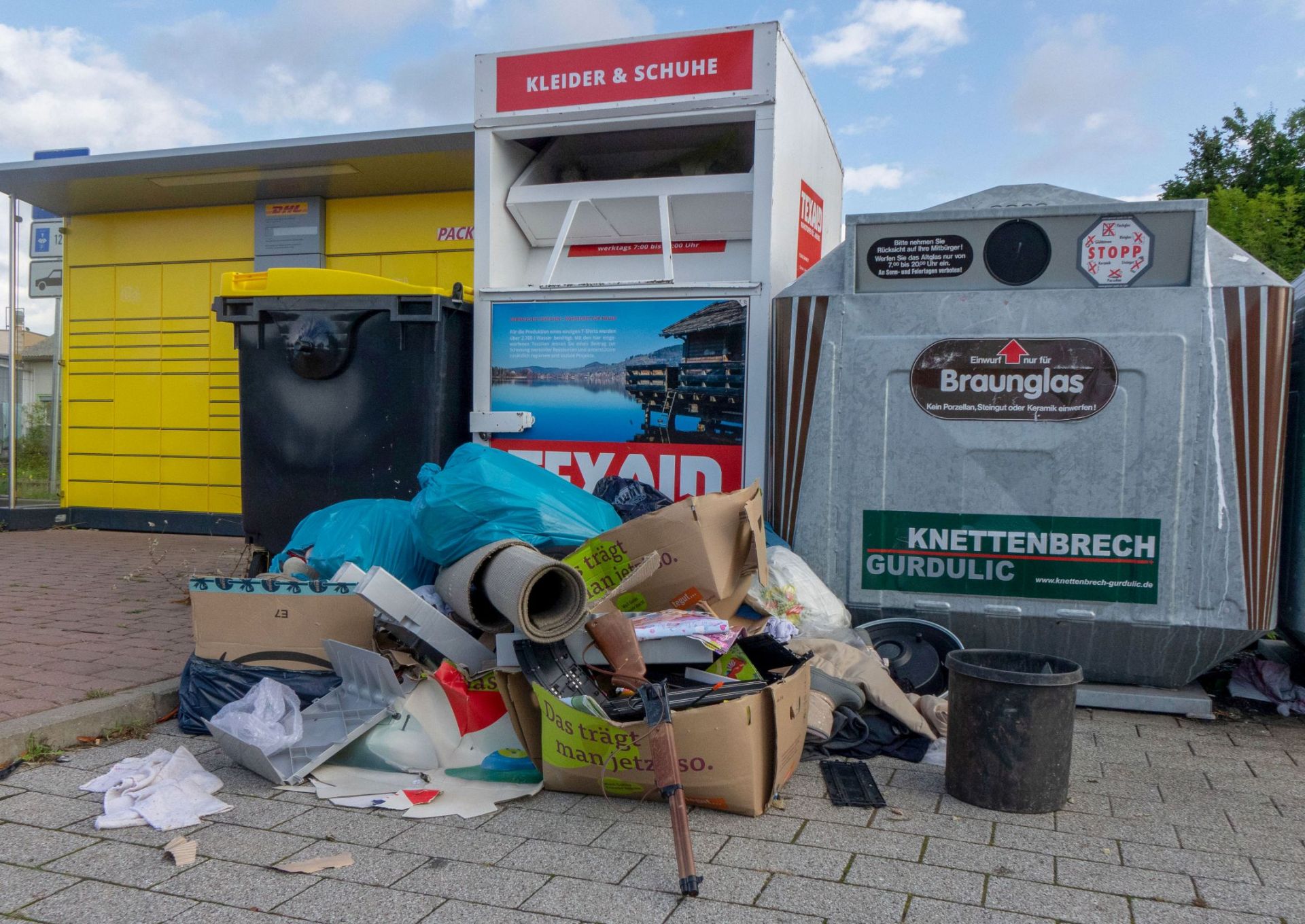 Vor den Sammelcontainern liegt eine größere Menge illegal entsorgter Abfälle.