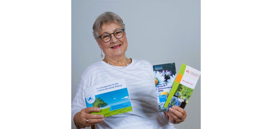 Johanna Abel war einige Jahre die Vorsitzende der Alzheimer Gesellschaft des Landkreises und verfügt über ein großes Wissen und Erfahrungen zu den Auswirkungen einer Demenzerkrankung auf den Freundes- und Familienkreis. Lächelnde Frau hält Informationsbroschüren zu Demenz, Beratungsangeboten und Unterstützungsmöglichkeiten für Betroffene und Angehörige in den Händen.