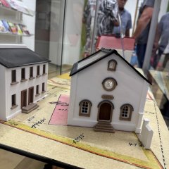 Zwei kleine historische Gebäudemodelle in einer Ausstellungsvitrine, im Hintergrund Besucher und Infotafeln
