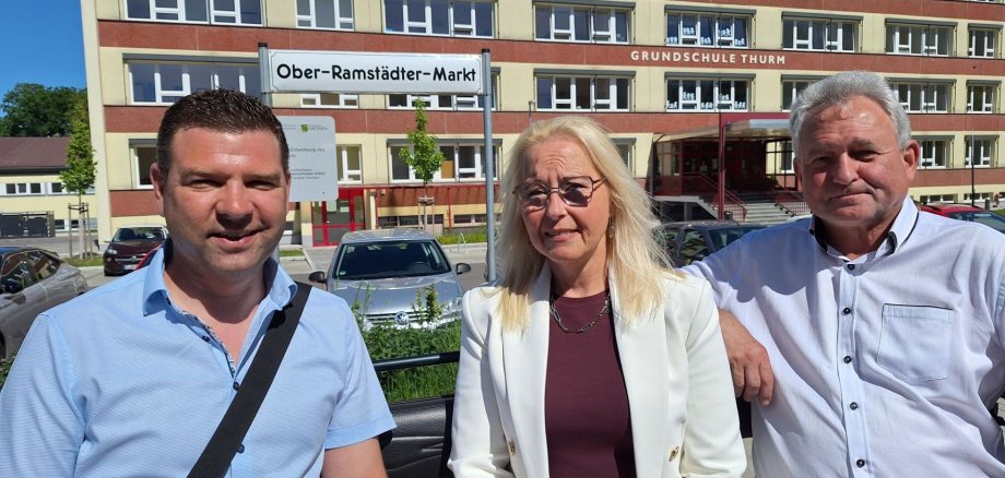 Rundfahrt durch die Gemeinde Mülsen Drei Erwachsene sitzen vor einem mehrstöckigen Schulgebäude mit der Aufschrift ‚Grundschule Thurm‘, während im Vordergrund ein Straßenschild mit dem Namen Ober-Ramstädter-Markt zu sehen ist