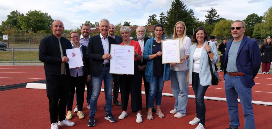 Hessische Kultusministerium der GCLS das Zertifikat „Gesundheitsfördernde Schule“ sowie das Teilzertifikat „Psychische Gesundheit“. Personen stehen zusammen bei der Übergabe eines Zertifikats