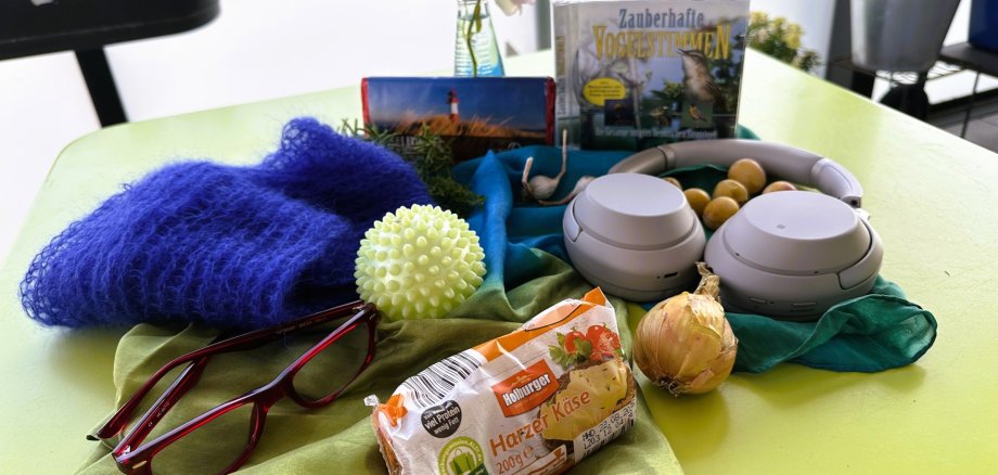 Die Blaue Stunde in der Petri-Villa Verschiedene Alltagsgegenstände – darunter Brille, Käse, Zwiebel, Kopfhörer und CDs – liegen auf einem gelbgrünen Tisch auf einem Balkon