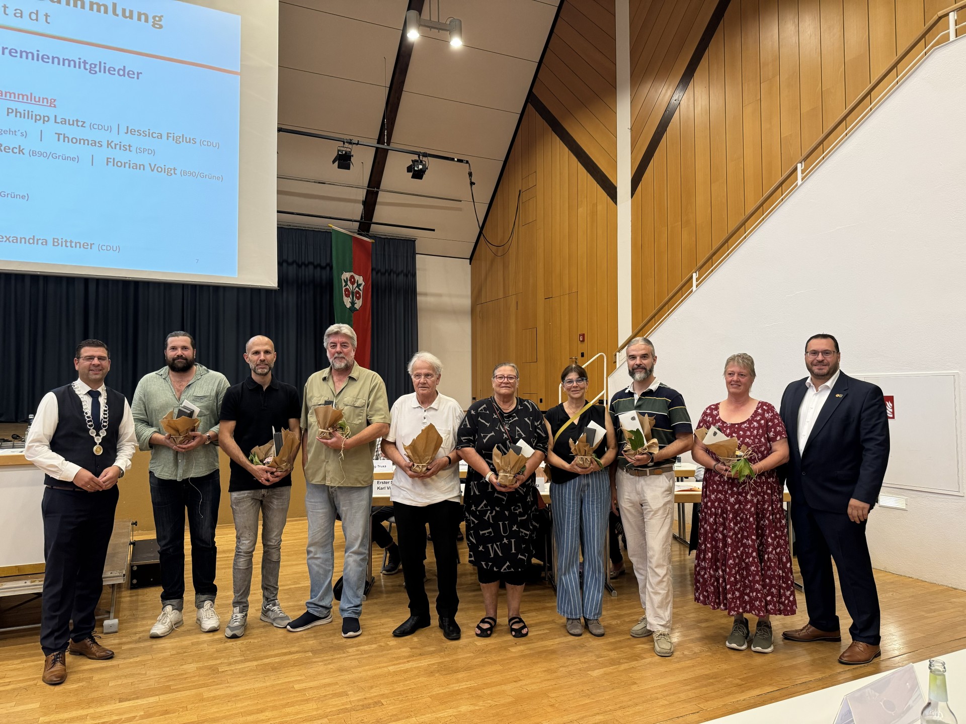 Gruppenfoto mehrerer Personen bei einer feierlichen Veranstaltung. Die Teilnehmenden stehen nebeneinander und halten teilweise Urkunden und Präsente in den Händen.