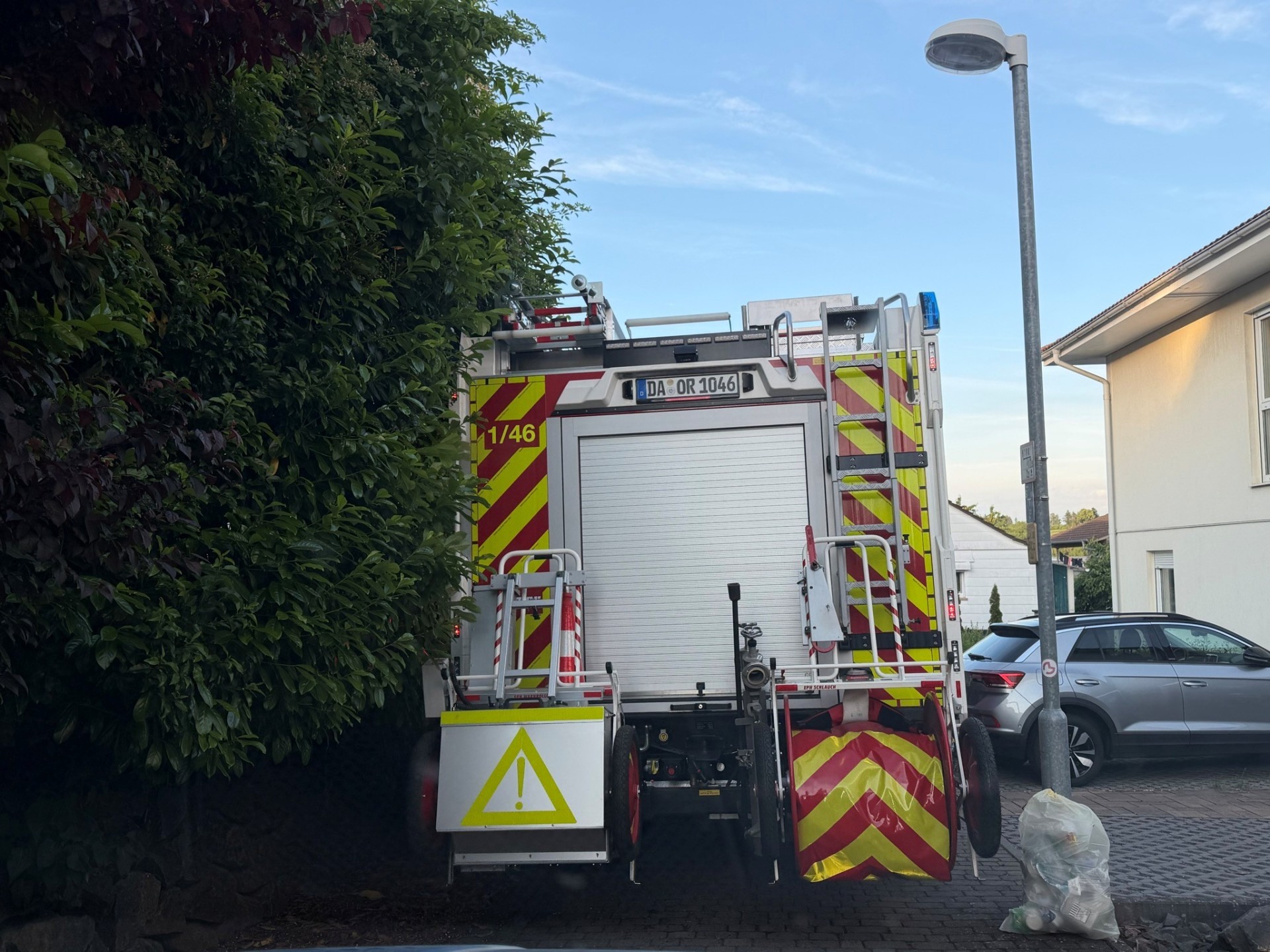 Feuerwehrauto im Einsatz Ein Feuerwehrfahrzeug steht rückwärts in einer engen Wohnstraße, dicht zwischen einer Hecke und einer Straßenlaterne.