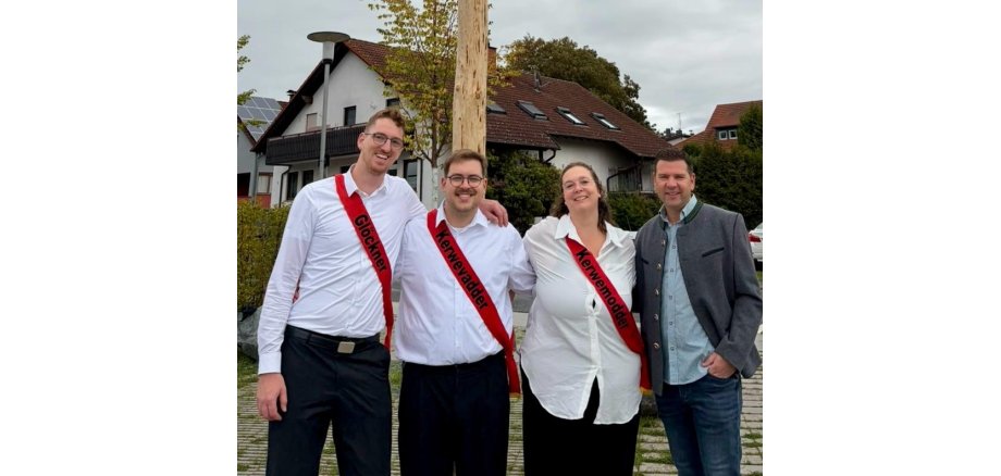 Vier Personen stehen lächelnd nebeneinander im Freien. Drei von ihnen tragen rote Schärpen mit den Aufschriften ‚Glöckner‘, ‚Kerwevadder‘ und ‚Kerwemodder‘.