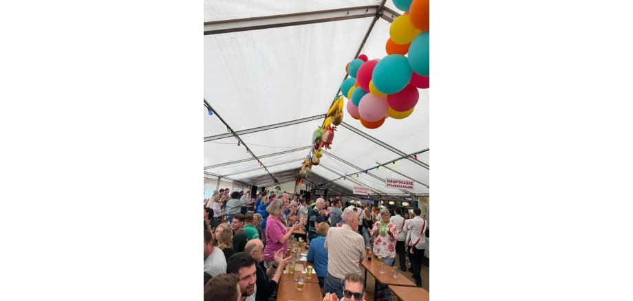 Die Stimmung im Festzelt am Kerbsonntag ist bestens. Viele Menschen sitzen und stehen an langen Holzbänken in einem Festzelt mit bunten Luftballons und genießen das Kerb-Programm.