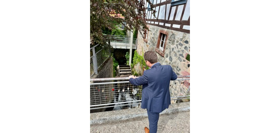 Begutachtung des Mühlraddes durch Bürgermeister Tobias Silbereis. Mann im Anzug blickt auf ein historisches Mühlrad an einem Fachwerkgebäude.