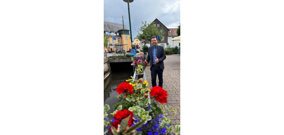 Bürgermeister Silbereis vor der schönen Bepflanzung entlang der Modau Lächelnder Mann im Anzug spaziert entlang eines mit Blumen geschmückten Bachlaufs durch einen Ortskern.